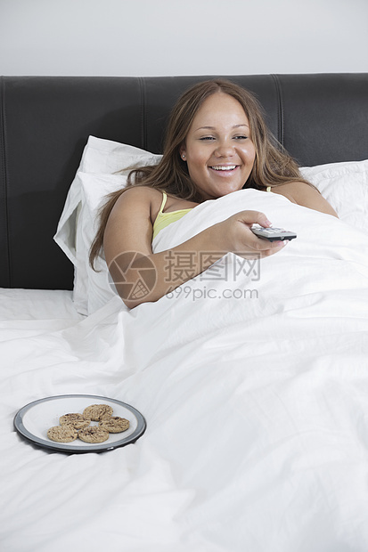 在家躺在床上时看电视的年轻快乐怀孕女青年妇女;图片