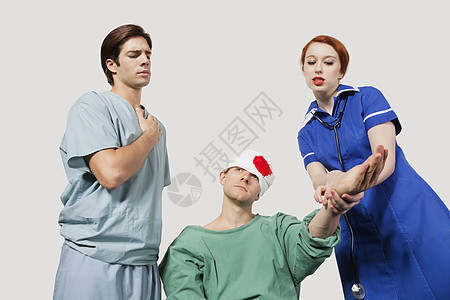 男医生兼女护士和女护士在灰色背景下治疗受伤病人图片