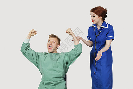 有女护士的男青年病人 在灰色背景下庆祝成功; 青男性患者和女护士图片
