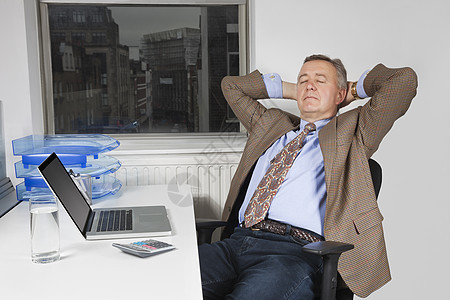 中年商务人士坐在办公室笔记本电脑前的椅子上图片