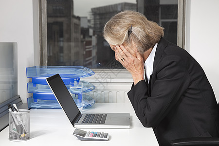 办公室办公台笔记本电脑前疲劳的高级女商务人士的侧面视图图片