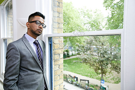 身戴眼镜站在窗边的印度商务人士肖像 在窗户旁站立图片