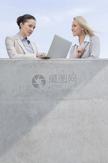 利用笔记本电脑与同事站在平台上对天站立的女商务人士低角度视图图片