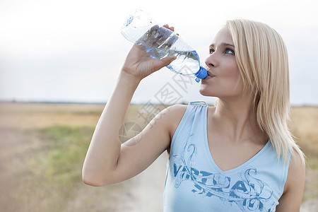 站在田地上时用瓶子喝水的漂亮女人图片