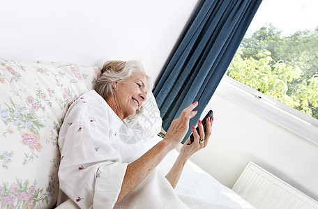 在家床上使用手机的快乐高龄妇女图片