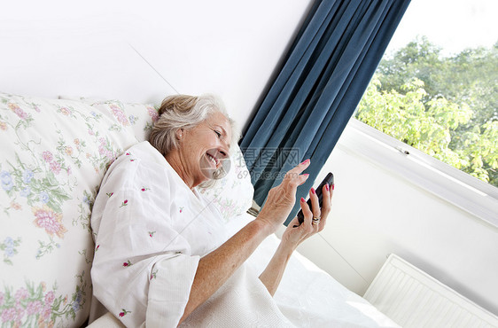 在家床上使用手机的快乐高龄妇女图片