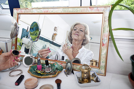 在家中喷洒香水的年长妇女的镜像反射图片