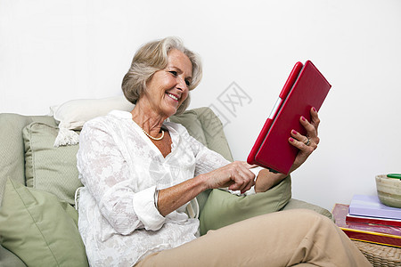 高级妇女在家里使用扶手椅上的数字片板图片