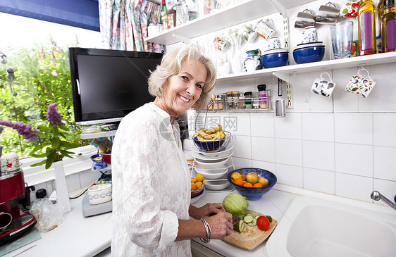 在厨房柜台切新鲜蔬菜的快乐老年妇女的画像图片
