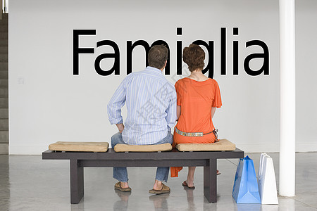 坐在长椅上的一对夫妇的近视 读意大利文本“Famiglia”(家庭)在墙上图片