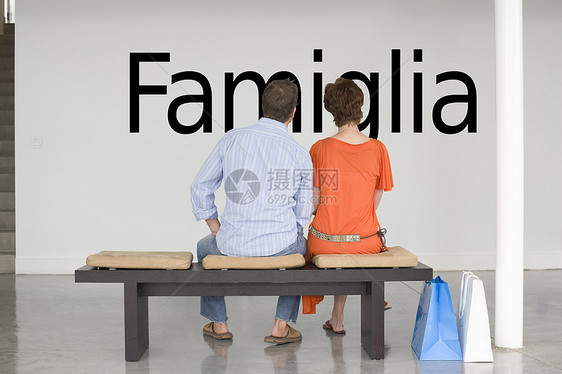 坐在长椅上的一对夫妇的近视 读意大利文本“Famiglia”(家庭)在墙上图片