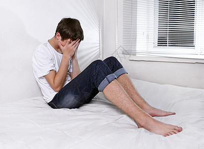 悲哀的年轻人在床边失败罪行床单伤害倾斜悲伤沙发牛仔裤男人焦虑图片