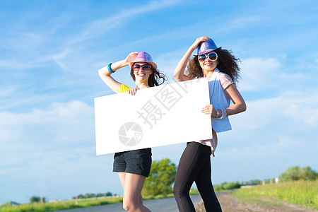 两名年轻女性站在空白的横幅上站着便车航程旅游女士女孩假期木板纸板天空成人图片