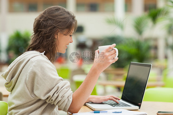 学生在食堂餐桌使用笔记本电脑时喝咖啡学习棕色夹克教育记事本学校桌子家庭作业女性大学图片