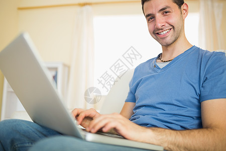坐在沙发上用笔记本电脑看照相机的人牛仔布技术公寓蓝色家庭住所客厅男人男性快乐图片