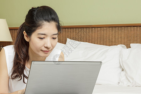 在卧室用笔记本电脑工作的年轻快乐的年青女士闲暇女性黑发女孩地面说谎冲浪技术互联网白色图片