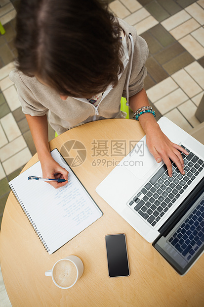 学生在餐厅桌旁用笔记本电脑做家庭作业饮料记事本短发杯子棕色学习头发键盘手机笔记图片