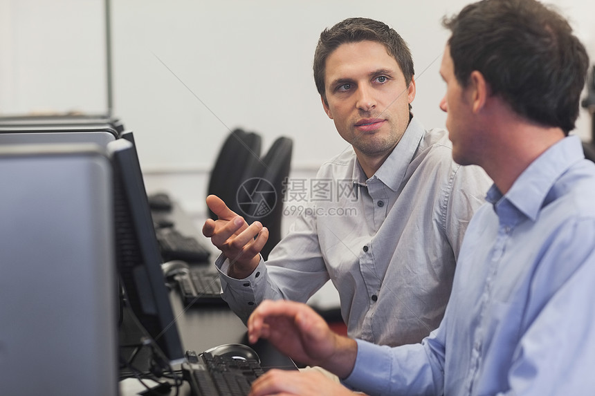 两个英俊的男人坐在电脑课上聊天时说话图片