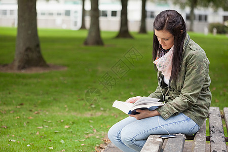 坐在长椅上看书的有焦点黑头发学生图片