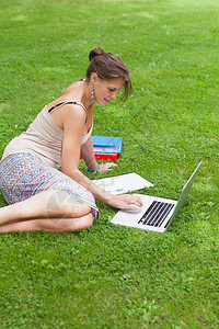 拥有笔记本电脑和公园书籍的女学生专注草原教育女性背心教科书头发学生裙子大学图片