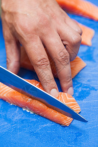 用尖刀割鲑鱼的手贴近图片