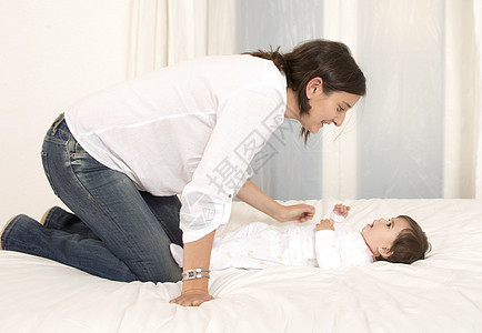 母亲和女儿在与世隔绝的床上玩耍母性妈妈牛仔裤拥抱微笑女性卧室头发投标育儿图片