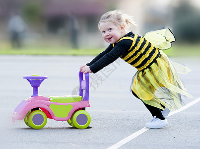 穿着蜜蜂服装的金发快乐女孩 推着玩具图片