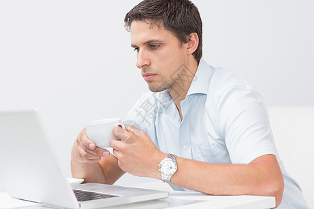 在家里用笔记本电脑打茶杯的严肃男人家庭生活茶几茶点饮料专注技术咖啡衬衫闲暇房子图片