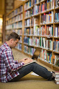 使用笔记本电脑坐在图书馆楼层的英俊年轻学生图片
