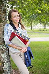 快乐的学生靠在树上拿着她的书图片