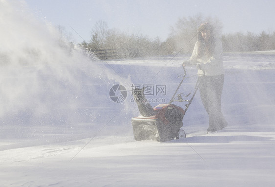 年轻妇女与吹雪者清扫车投掷者季节冷冻车道降雪机器工作打扫女士鼓风机图片