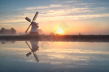 日出时在河流中反射的荷兰风车图片