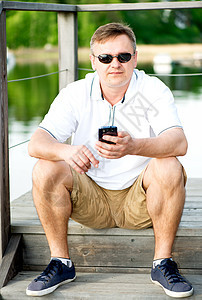 在码头坐着戴太阳眼镜的成熟男子自由树木男性闲暇孤独反射中年娱乐眼镜码头图片