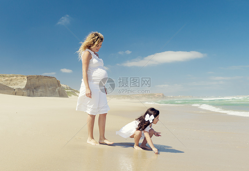 孕妇和她女儿在沙滩上的海滩上天空妈妈父母母性连衣裙假期童年孩子们微笑女孩图片