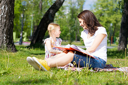女孩和年轻女子一起阅读一本书绘画老师托儿所成人公园快乐后院场地学习女士图片