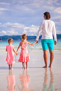 热带白沙滩上两个小女孩和年轻父亲的背面景象乐趣幸福孩子父母海滩女儿海岸情调女孩男人图片