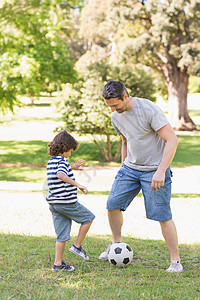 父亲和儿子在公园踢橄榄球男人微笑家长学习教学运动爸爸孩子家庭足球图片