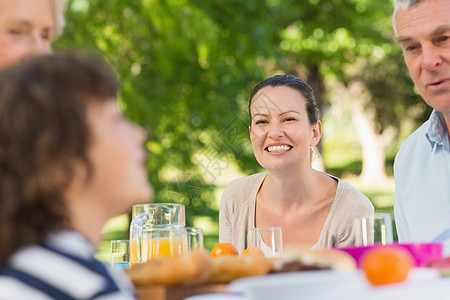 与家人一起坐在户外餐桌上的妇女老年公园享受儿子团结花园桌子草地用餐家庭图片