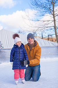 年轻快乐的父亲和可爱的小女孩 在滑冰场上活动手套家庭训练教育学习女儿女孩帮助溜冰者图片