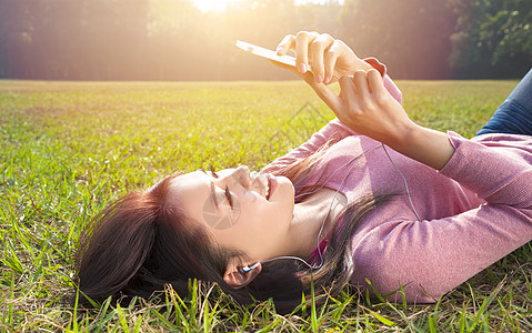 微笑的年轻女子触摸手机和躺在草地上图片