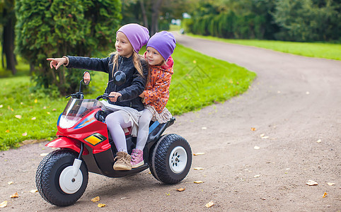 坐在绿色公园的玩具摩托车上坐着的小可爱姐妹自行车游戏快乐喜悦孩子乐趣婴儿运输活动女孩图片