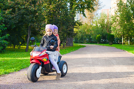 可爱的小女孩 在绿色公园骑着孩子的摩托车自行车夹克速度喜悦运输运动玩具快乐微笑游戏图片
