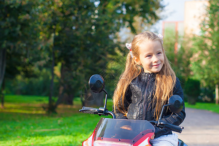 穿着皮夹克的快乐小摇滚女孩的肖像 坐在玩具摩托车上阳光喜悦自行车乐趣娱乐童年情感姐姐游戏运输图片