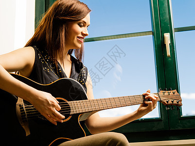 微笑的女人在窗边弹吉他图片