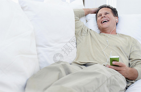 男人在客厅沙发上听MP3播放器耳机享受活动男性中年休闲家具音乐音频服装图片