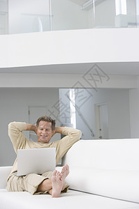 沙发上有笔记本电脑的中年男子头发微笑享受房子棕色技术图片