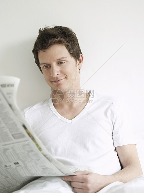 年轻男子在床上看报纸和微笑图片