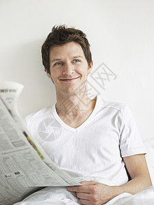 年轻男子在床上看报纸 一边看着一边笑着微笑场景快乐一人活动家庭生活短发卧室男人头发羽绒被图片