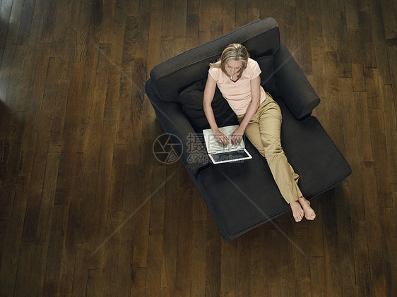 使用上方笔记本电脑视图坐在沙发上的中成年妇女图片
