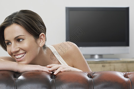 在沙发上当着平板屏幕电视的女青年微笑客厅成人男人真皮倾斜女性成年一人摄影图片